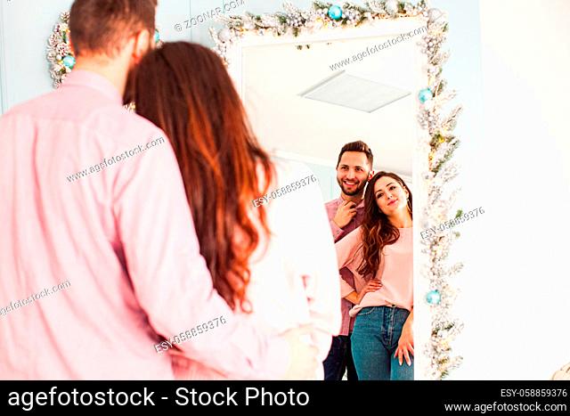 Romantic couple look at designed mirror with Christmas decoration. Preparation for New Year Party
