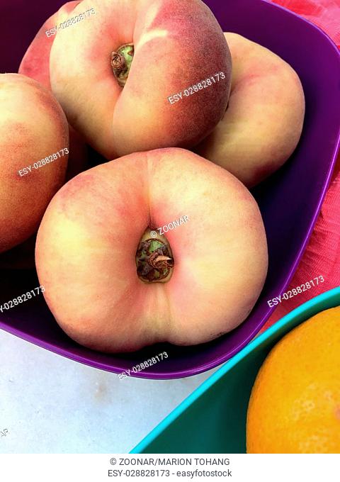 Fresh doughnut peaches fruits in a purple bowl
