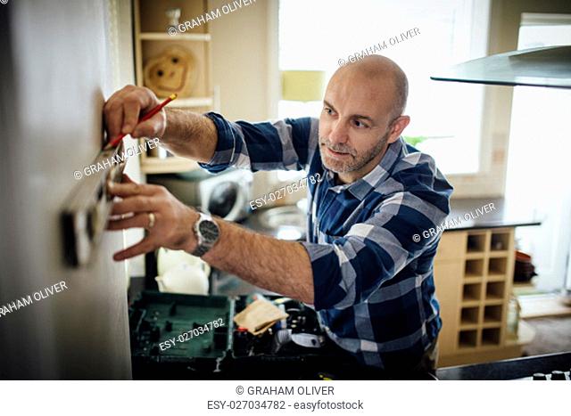 Mature man using a spirit level and marking the wall with a pencil in his kitchen