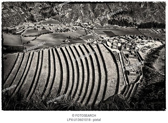 Pisac ruins: detail monochrome view of agricultural terracing and Inca citadel, with modern town beyond, Sacred Valley, Cuzco, Peru