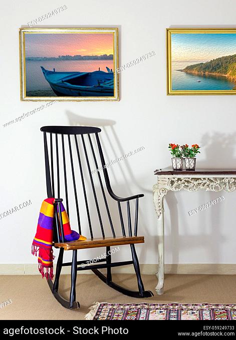 Classic rocking chair and two old books on old style vintage table on background of off white wall with two hanged paintings with clipping path for paintings