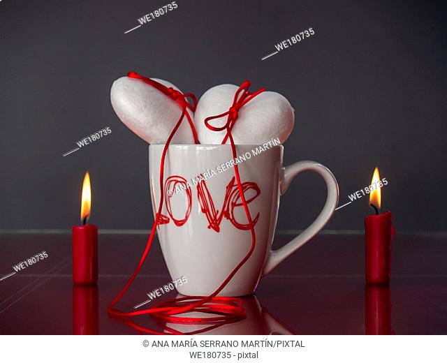 Concept of love Two poliespan hearts joined with a red thread that symbolizes the legend of the red thread on a breakfast cup and two red lit candles