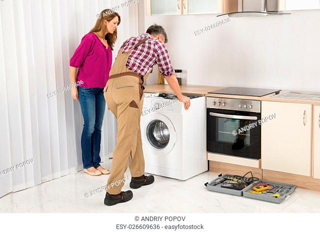 Mature Woman Looking At Male Worker Repairing Washing Machine In Kitchen