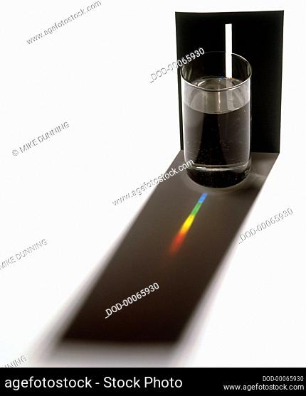 Light beam through glass of water and colour spectrum on black shadow