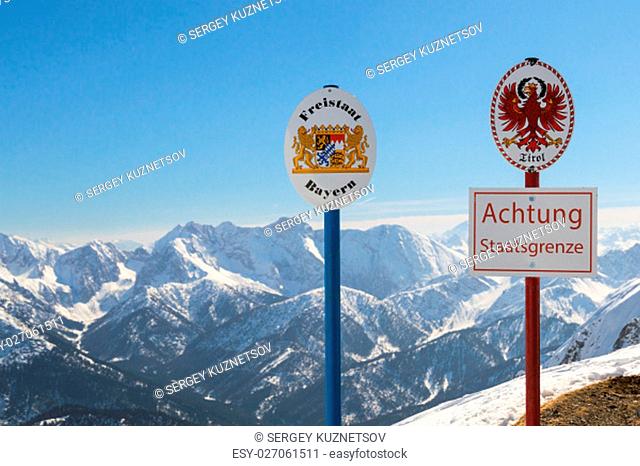 State boundary between Germany and Austria on top of Alpine mountain ridge. Sgnboards with the coat of arms of free state Bavaria and Tyrol and words ""Warning:...
