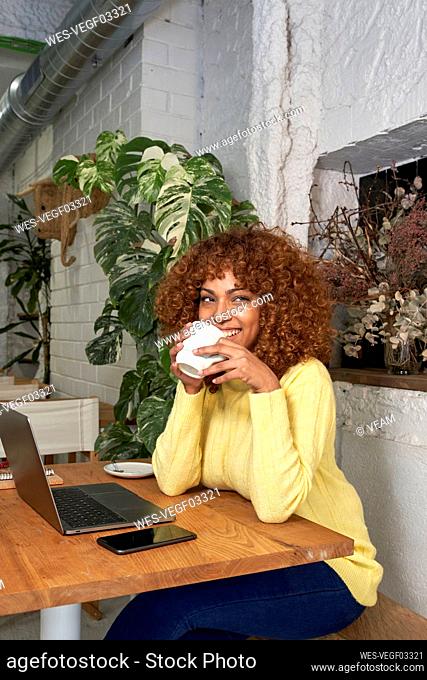 Happy female entrepreneur having coffee while looking away in coffee shop