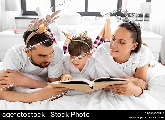 family with book in pajamas in bed on christmas