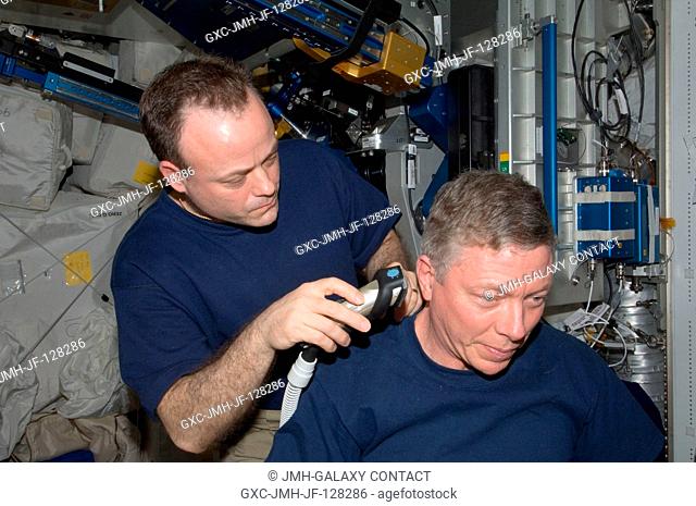 NASA astronaut Ron Garan, Expedition 28 flight engineer, trims astronaut Mike Fossum's hair in the Tranquility node of the International Space Station