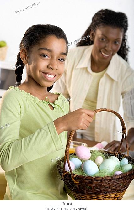 Portrait of girl holding Easter eggs in basket with mother looking at her