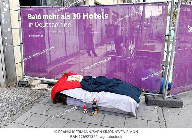 Sleeping a homeless person with blankets on polystyrene panels on a sidewalk withten in Munich in front of a construction site in the city center behind a...