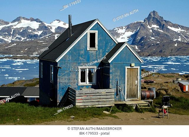 Old blue painted house in front of fjord with ice pack and snow-capped mountains Ammassalik Eastgreenland