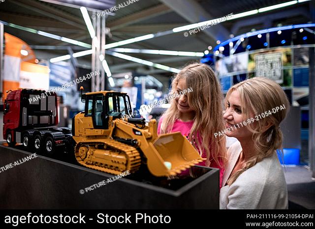 16 November 2021, North Rhine-Westphalia, Dortmund: Model Emilia and Anna (l-r) look at a model of an excavator. The Dortmund fair and the Federal Association...