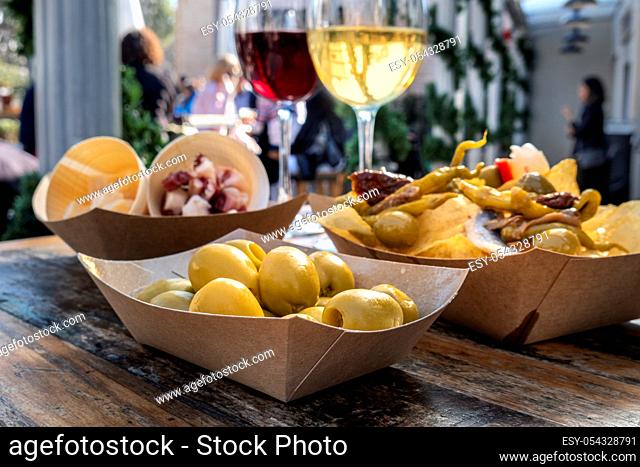 Tapas bar. Olives, potato chips, cheese and jamon, red and white wine, on a wooden table in an outdoors cafe