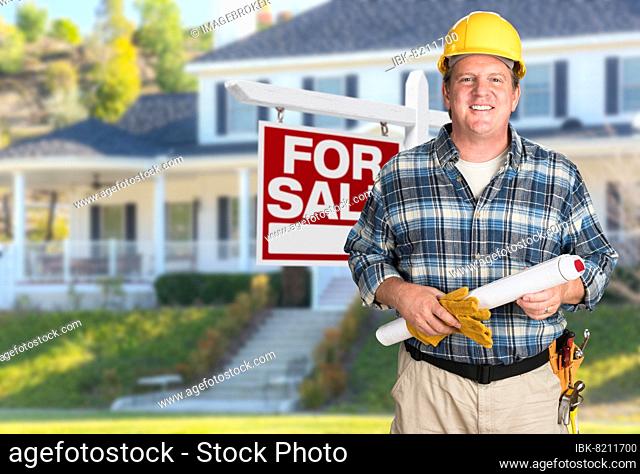 Contractor with plans and hard hat in front of for sale real estate sign and house