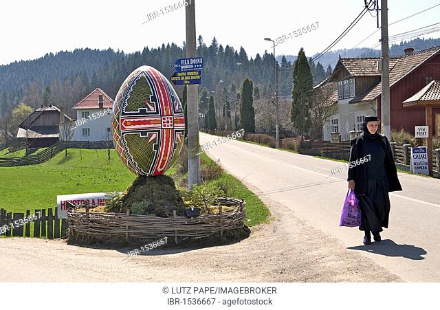 Nun, oversized Easter egg as a sign to the Moldova convent, Voronet Monastery, Eastern Carpathians, Romania, Europe