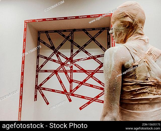 A man in a mummy suit on background of the logo supreme. Theme style and fashion. Halloween Costume Party. in makeup woman in bandages and clay is like a mummy...