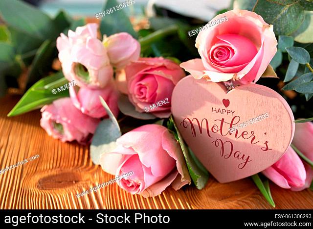 Mothers day card with pink spring flowers and heart shape on rustic wood. Close-up with short depth of field and english text