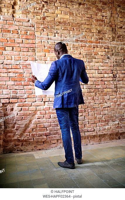 Businessman studying plan at brick wall