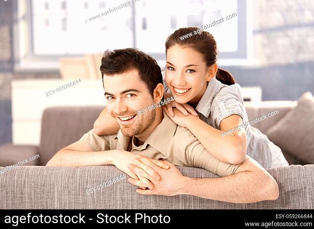 Young couple smiling happily on sofa, hugging each other at home