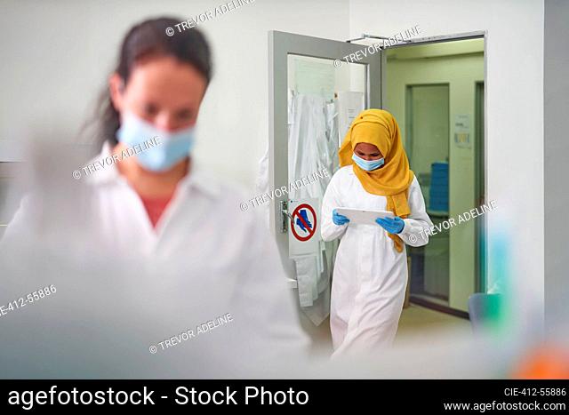 Female scientist in face mask and hijab using digital tablet