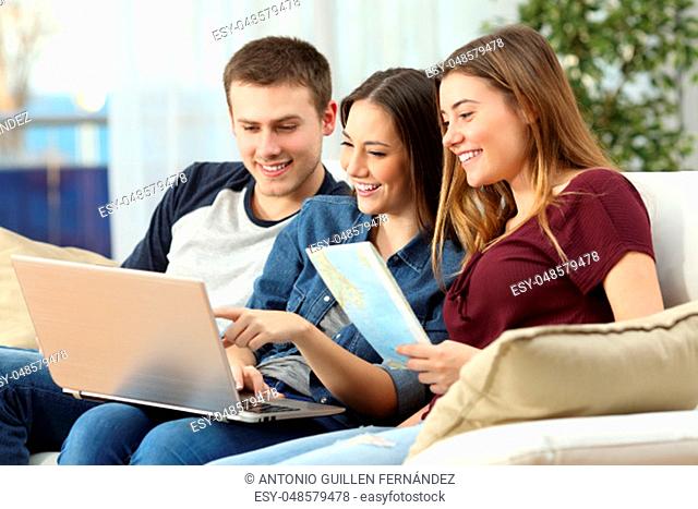Three friends planning a trip with a laptop and a paper map on line sitting on a sofa in the living room at home