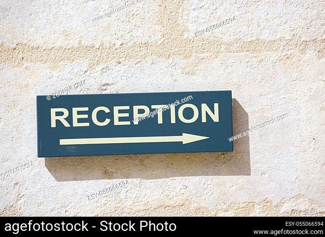 Closeup on sign attached to a white wall indicating where the reception area is