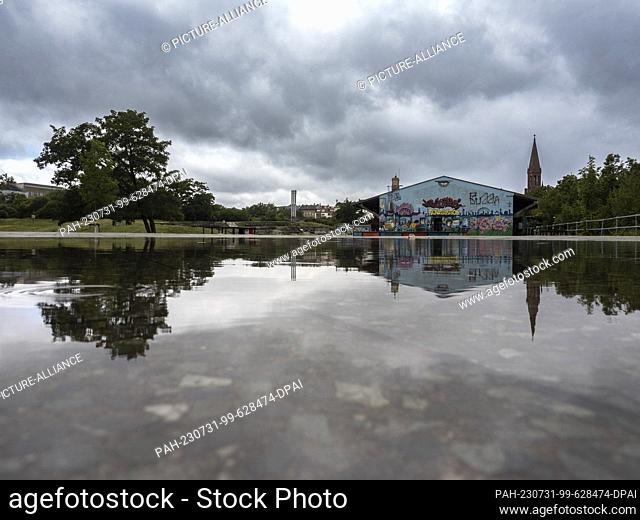 31 July 2023, Berlin: Dark clouds are reflected in a puddle of rain in Görlitzer Park. The green space in Kreuzberg is always a source of discussion