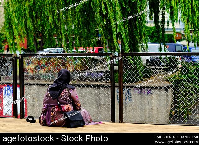 15 June 2021, Berlin: A woman in a headscarf looks out over the Landwehr Canal as she sits on a wooden terrace on Maybachufer