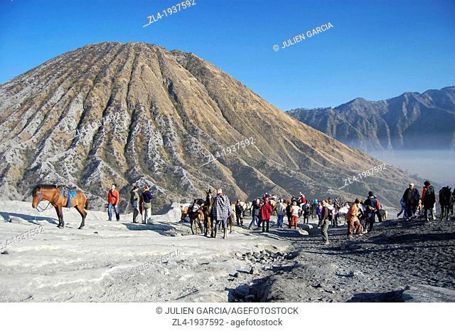 Tourists, locals and horses at the foot of mount Bromo. Mount Batok in the background. Indonesia, Java, Jawa Timur, Bromo-Tengger-Semeru National Park