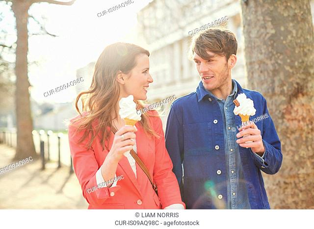 Couple eating ice cream cones whilst strolling along street, London, UK