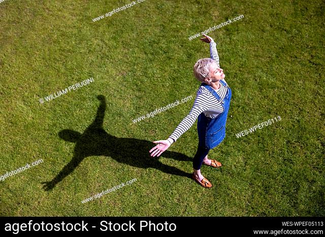 Mature woman with arms outstretched on grass during sunny day