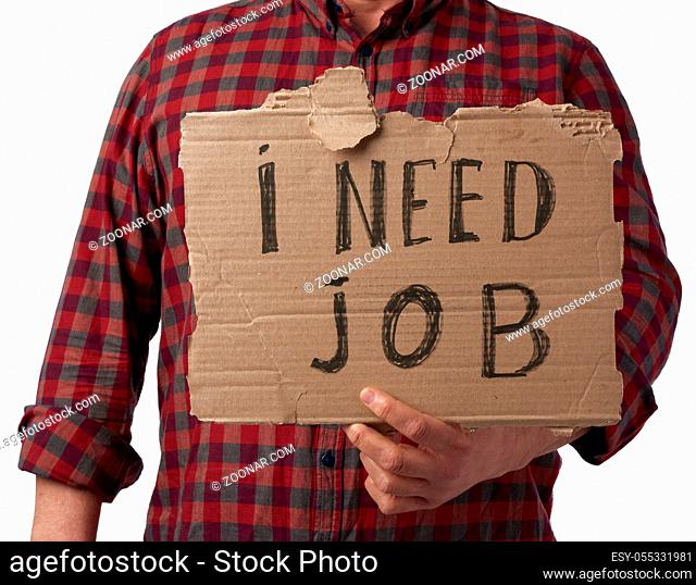 man in a plaid shirt and jeans holds a piece of paper with the inscription i need job, concept of unemployment against the backdrop of the global crisis