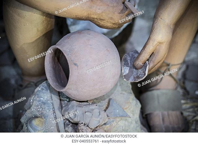 Life-sized sculpture of prehistoric man decorating clay bowl