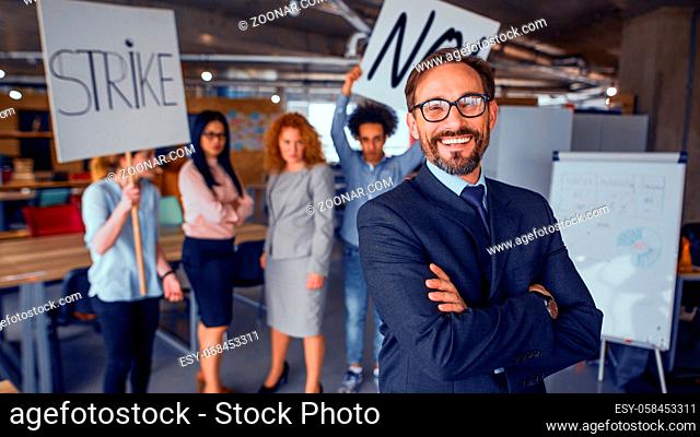 Modern office concept, director standing with his back to striking cowokers. unhappy employees holding posters with words strike and no. Toned concept