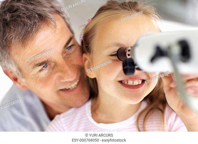 Cute young girl looking at sky through telescope with her father