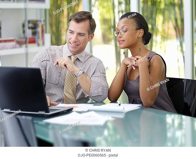 Two businesspeople in an office looking at a laptop