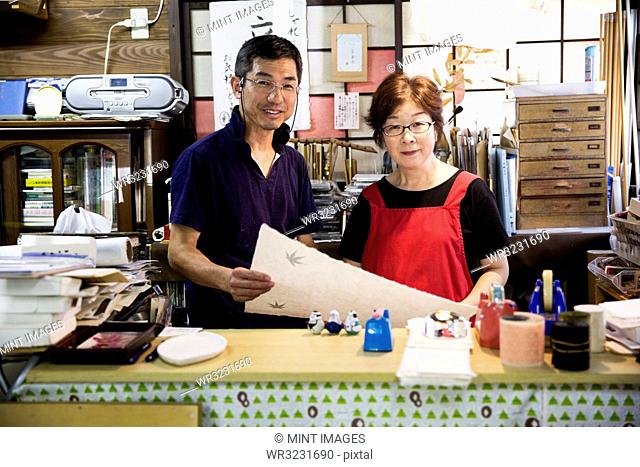A man and woman, partners in a traditional business, behind a counter in a shop, displays of traditional handmade fibre washi paper