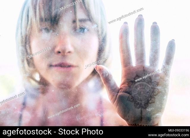 Peace and hippy spiritual meditation concept with young pretty girl behind a glass with palm of hand on tthe glass and mandale indian style designed in - bright...