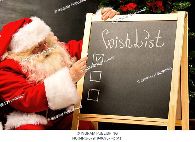 Santa Claus sitting near chalkboard with wishlist sign and blank copy space for checkboxes and your text