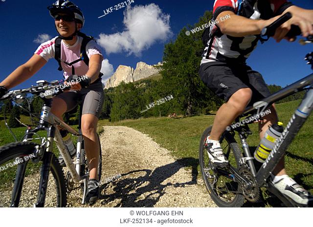 Young couple riding mountain bikes under blue sky, South Tyrol, Italy, Europe