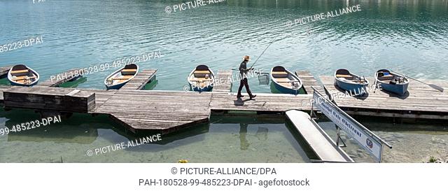 28 May 2018, Germany, Walchensee: A man walks across a footbridge with his fishing rod at the shore of Walchensee (Lake Walchen)