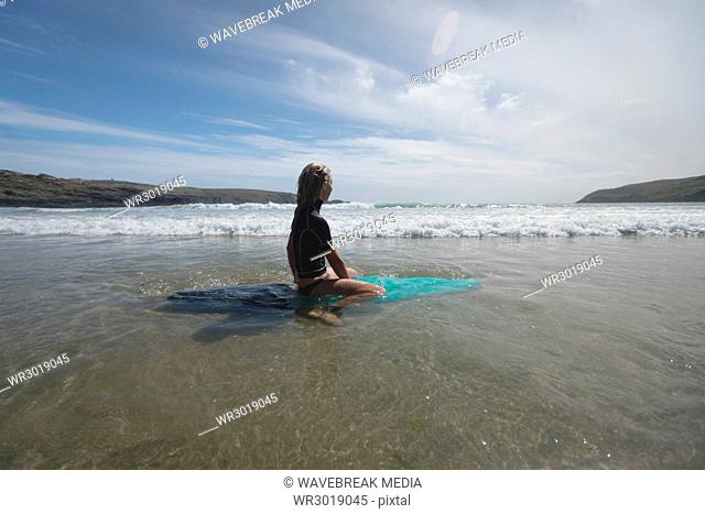 Woman sitting on surfboard looking at the sea