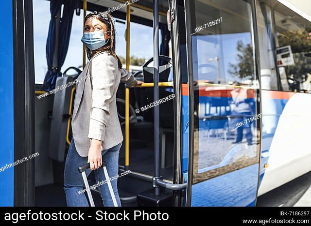 Young woman with luggage and protective mask boarding to the bus in Faro, Portugal, Europe