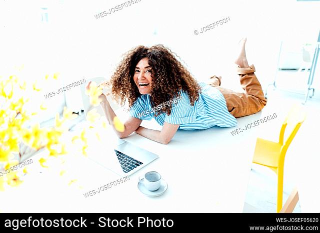 Cheerful businesswoman with laptop lying on table in office