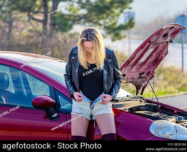 Young blonde woman undressing denim hot-pants before broken car
