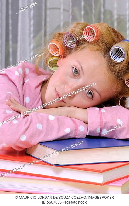 Redheaded woman wearing pajamas with curlers in her hair leaning over a stack of books