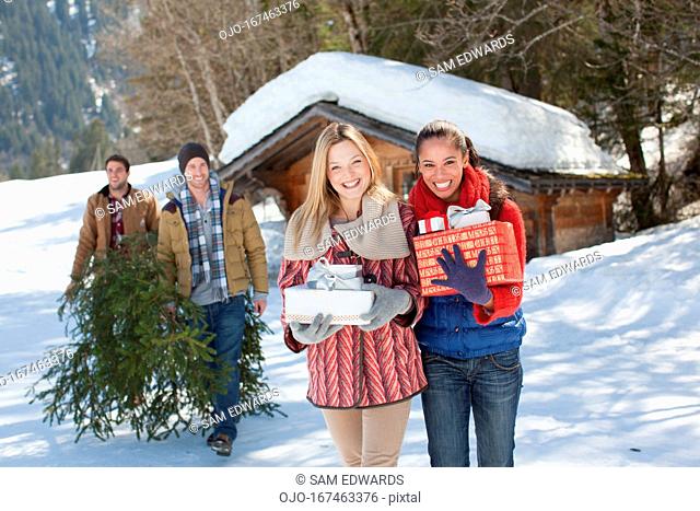Portrait of smiling couples with fresh cut Christmas tree and gifts in snow