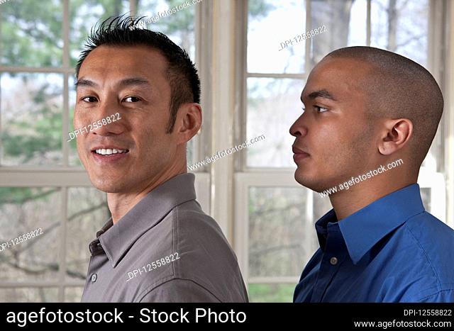 Portrait of the side view of two young businessmen standing facing left, one looking at the camera