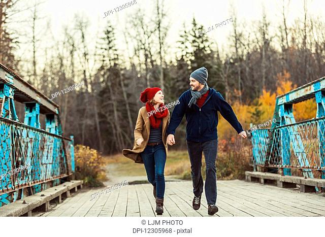 A young couple running on a bridge during the autumn season in a city park; Edmonton, Alberta, Canada