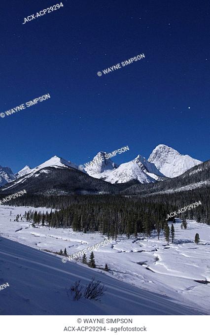 The Rocky Mountains illuminated by a full moon on a winter night in Spray Valley Provincial Park in Kananaskis Country, Alberta